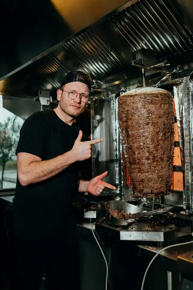 Mitarbeiter von Honest Kebab zeigt auf den Dönerspieß in der Küche.