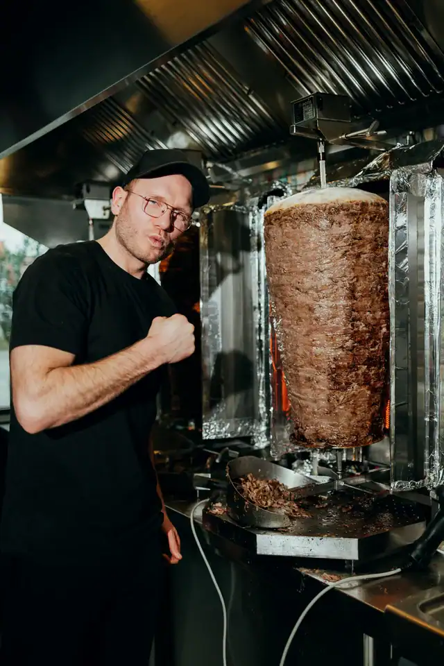 Mitarbeiter von Honest Kebab zeigt auf den Dönerspieß in der Küche.