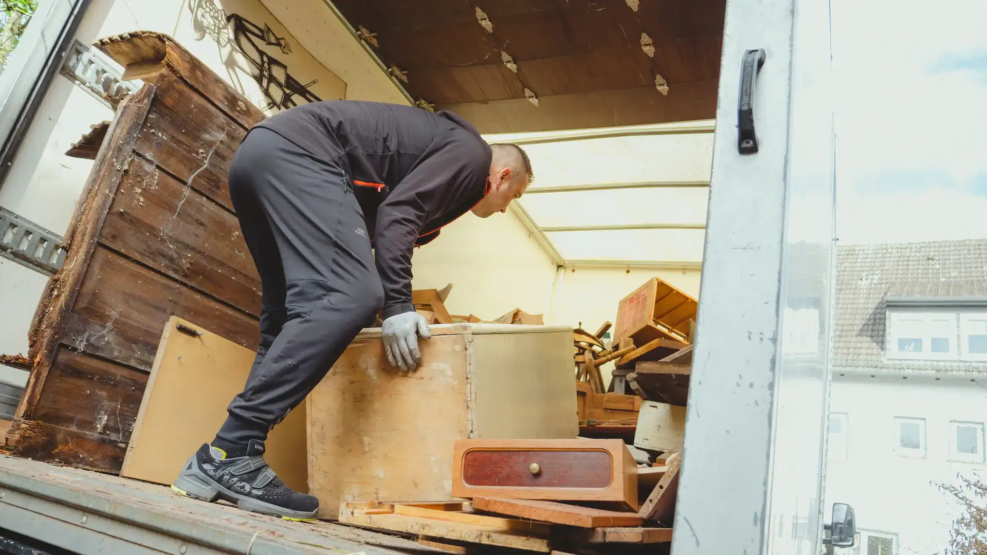 Mitarbeiter verstaut alte Möbel auf der Ladefläche eines Transporters.
