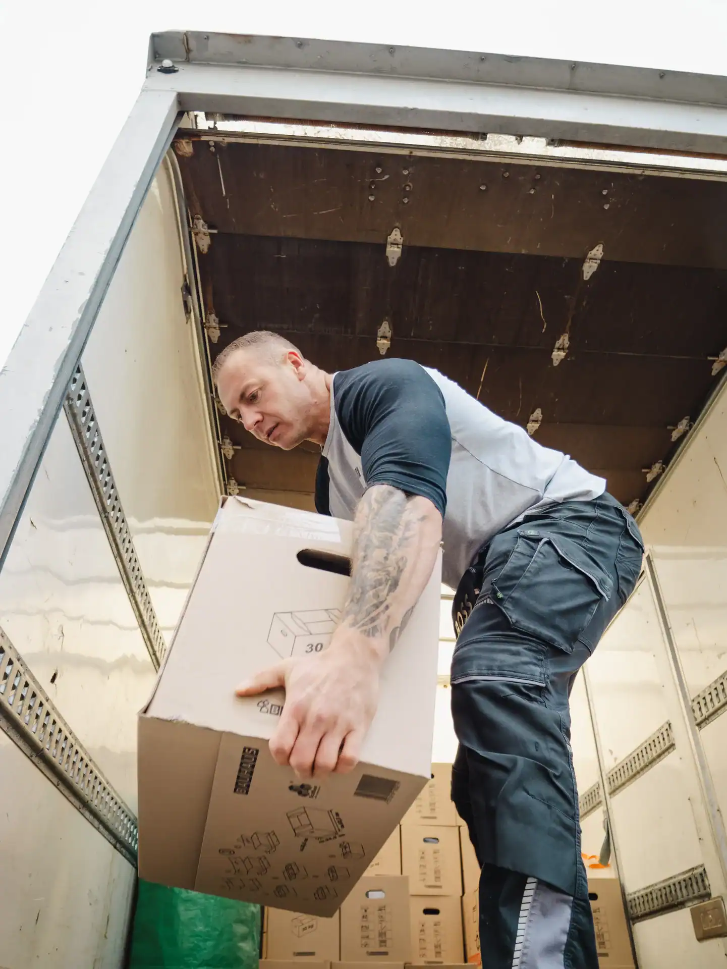 Mitarbeiter hält einen Umzugskarton auf der Ladefläche eines Transporters